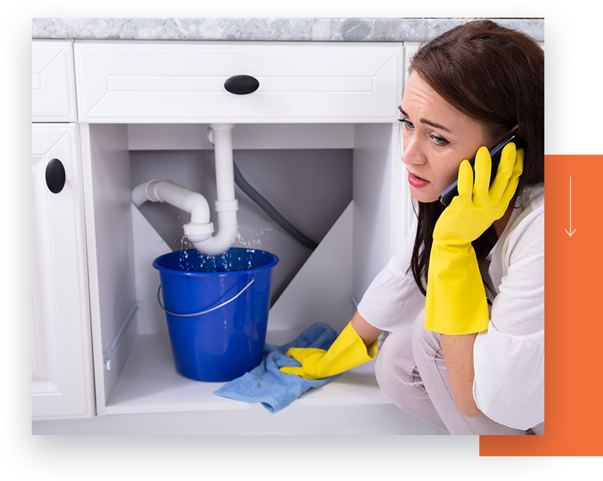 A worried woman on the phone with a bucket under a leaking pipe